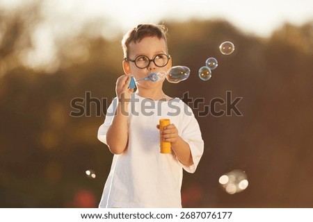Blowing bubbles. Boy is having fun on the field under sunlight at daytime.