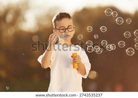 Blowing bubbles. Boy is having fun on the field under sunlight at daytime.