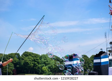 Blowing hundreds of tiny, small and big bubbles at outdoor festival in city center next to harbor, ships. Concept of entertainment, birthdays. Kids having fun. Shower of bubbles flying in blue sky.
