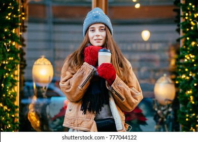 Blown away dreaming woman drinking coffee outdoor in winter city street over beautyful shop window. Christmas, new year, winter holidays concept. - Powered by Shutterstock