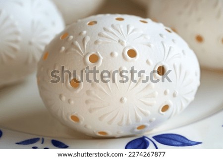 Blown white Easter egg decorated with wax oraments with drilled holes