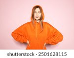 Blows a bubble out of chewing gum Woman Posing, Orange Hoodie on Pink Background