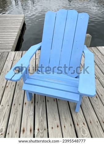 A blue Adirondack chair sitting on a dock by the water.