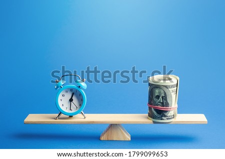 Blue alarm clock and a bundle of dollars on scales. Fair hourly wages. Time tracking. Deposit, money investment. Profitability and return on investment. Rental. Balance between life and career.