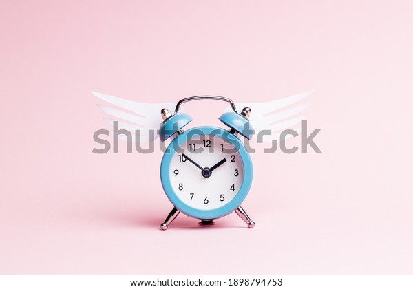 blue alarm clock with origami wing over pink\
pastel background. valentine romance day concept. greeting card\
template.