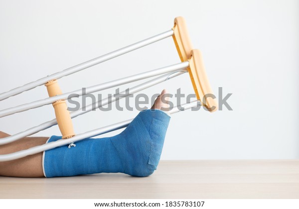 Blue ankle and foot splint Bandages on\
the legs from a young man\'s fall accident, Blue plaster on the\
ankle, Crutches assist in the walking of the\
patient.