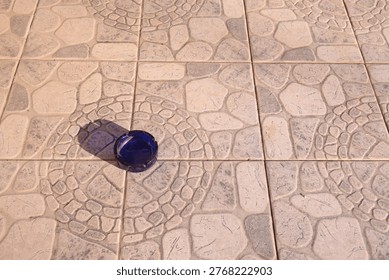Blue ashtray casting shadow on patterned stone tile floor.