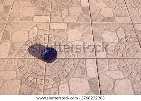 Blue ashtray casting shadow on patterned stone tile floor.