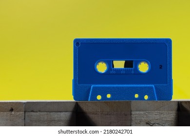 A Blue Audio Cassette On A Wood Surface Against A Yellow Background In A Studio Environment