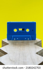 A Blue Audio Cassette On A Wood Surface Against A Bright Yellow Background In A Studio Environment