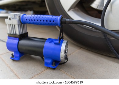 Blue automobile compressor, standing next to the car wheel. Electric air pump inflates the tire, repaired after puncture. Selective focus