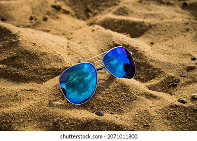 Blue aviator sunglasses on a sandy beach