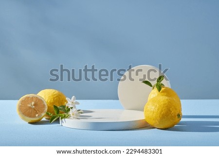 Blue background with fresh lemons, white flower and round podium. Blank space for display product of lemon ingredient. Lemon has many good uses for health and beauty.