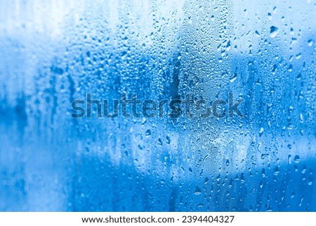 Blue background of glass of metal-plastic window with water droplets condensation indoors room. High humidity. Moisture condensation problems, hot water vapor condensed on window in cold season