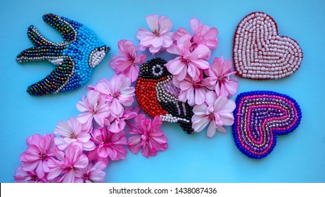 Blue background with handmade beadwork elements - swallow and bullfinch birds, pink geranium flowers, colorful hearts