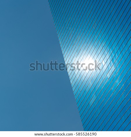 Blue background. The left side is blue sky, the right half is a modern blue glass office building with a spot that is reflection of the sun. Space for text. Fine for placing logo in the center