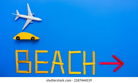 Blue Background With Toy Airplane, Yellow Wooden Car And Text Beach With Red Arrow From Above