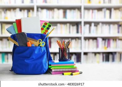 Blue backpack with school supplies on wooden table against blurred book shelves. School concept. - Powered by Shutterstock