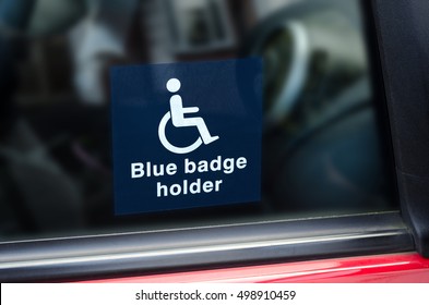 Blue Badge Holder Sign. White And Blue Sticker With A Wheel Chair Symbol On Stuck To The Inside Of A Car Window. 