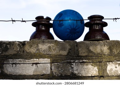 Blue ball with sun pattern between ceramic electrical insulators on brick wall behind barbed wire, conceptual background. The shot has strong conceptual and symbolic meaning due to the combination of barbed wire, closed barriers and bright ball with sun and star patterns.