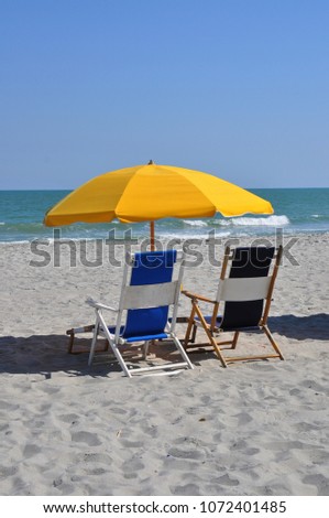 Blue beach chairs and yellow sun umbrella at the seashore.
