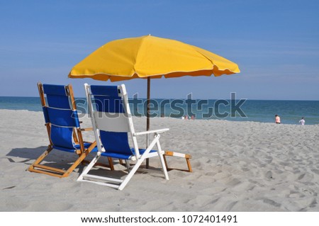 Blue beach chairs and yellow sun umbrella at the seashore.