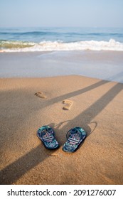 Blue Beach Slippers On A Sandy Beach. Footprints Of A Man On The Shore. Rest By The Sea, Summer Adventures. Surf Noise And Sea Foam. High Quality Photo