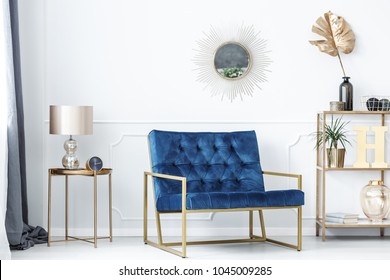 Blue bench between gold table with lamp and shelves with leaves in glamor living room interior - Shutterstock ID 1045009285