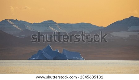 Blue berg, yellow cliffs; Blue bergs and mountains at evening; Scoresby Sund, Greenland