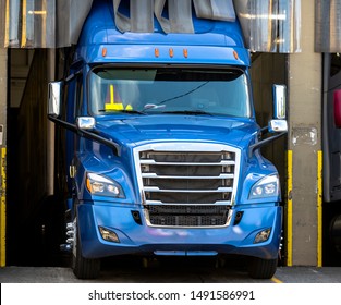 Blue Big Rig Beautiful Shape American Powerful Semi Truck With Chrome Accents And Refrigerated Semi Trailer Standing In Warehouse Dock Space For Loading Frozen Cargo For Next Delivery