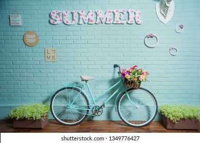 Blue bike on brick wall background. Summer photo zone in the Studio. Wicker basket with artificial flowers on the bike.