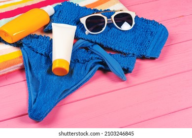 Blue bikini with sunblock cream bottle on bright pink wooden background