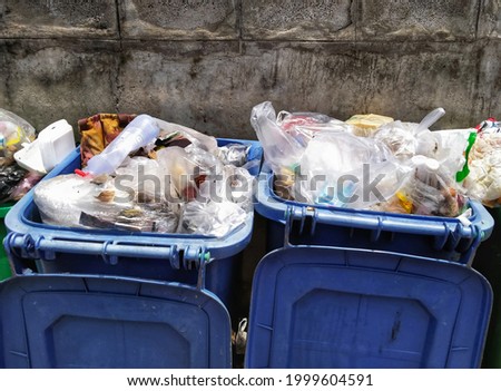 Blue bins, overflowing garbage, unsorted garbage, trash bins behind the concrete wall