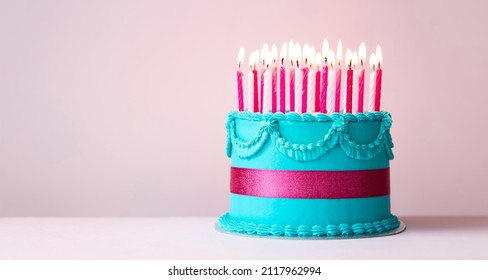 Blue birthday cake with buttercream piping, pink ribbon and pink birthday candles - Shutterstock ID 2117962994