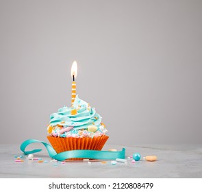 Blue Birthday Cupcake With Orange Candle Over Grey