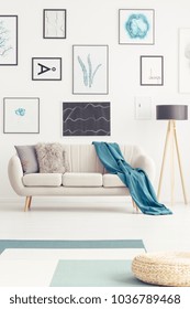 Blue blanket on a settee next to a lamp in living room interior with pouf and gallery of posters - Shutterstock ID 1036789468