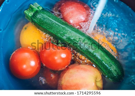 Blue bowl full of fruits and vegetables with tap water and lye in the kitchen sink. Disinfecting fruit and vegetables to prevent the spread of the coronavirus.