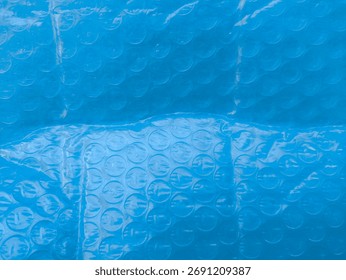 Blue bubble-wrap macro with repeating air cells, a playful grid of circles catching highlights and shadows—the familiar cushioning film turns graphic and abstract, its cool tone and tactile pop render