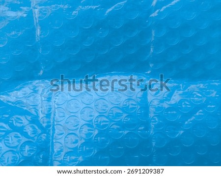 Blue bubble-wrap macro with repeating air cells, a playful grid of circles catching highlights and shadows—the familiar cushioning film turns graphic and abstract, its cool tone and tactile pop render
