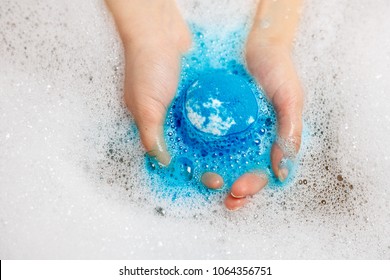 Blue bubbling ball of bath salts in hands. Bomb for the bath. Blue hands. Blue water with foam. Closeup. It dissolves in the hands.