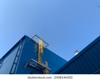 A blue building with a yellow metal ladder going up the side of the building. - Powered by Shutterstock