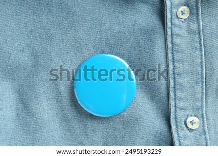 Blue button badge pinned on denim shirt, top view. Mockup for design