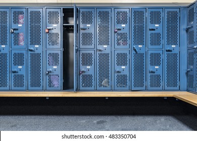 Blue cage lockers in a gym with a bench in front 