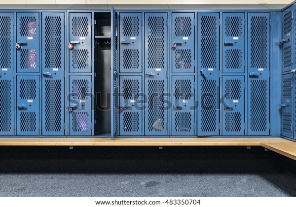 Blue cage\
lockers in a gym with a bench in front\
