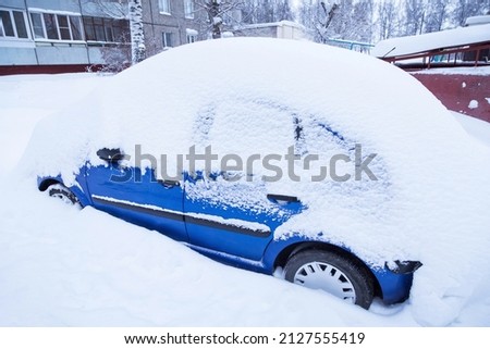 Blue car covered snow on winter town street after snowfall	