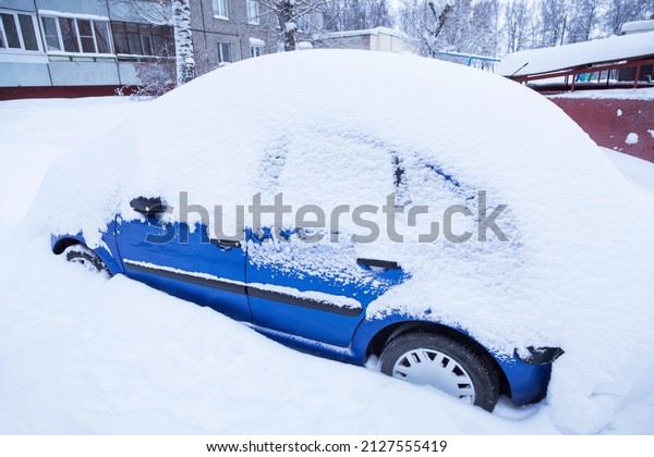 Blue car covered snow on winter town street\
after snowfall	