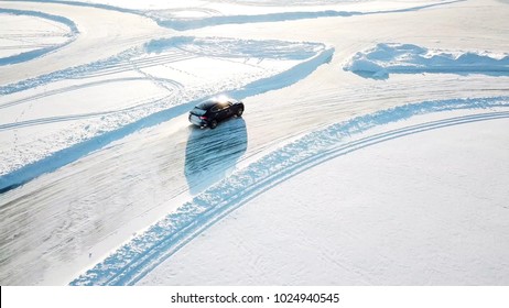 Blue Car Drives By Icy Track On Snow Covered Lake At Winter. Aerial View. Sport Car Racing On Snow Race Track In Winter. Driving A Race Car On A Snowy Road.