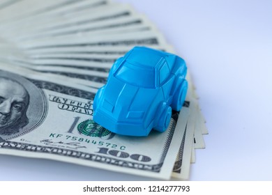 A Blue Car Figure Stands On A Table Covered With Hundred Dollars Bills. Concept For Advertising Loan, Collateral, Pawnshop, Car Rental. Money Cars Concept Or Idea.