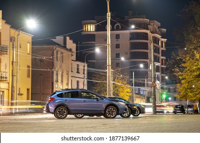 Blue Car Parked On Brightly Illuminated City Street At Night.