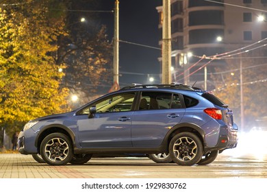 Blue Car Parked On Brightly Illuminated City Street At Night.